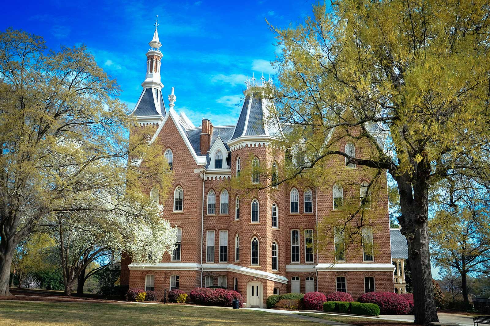 A stately brick building nestled among trees with a blue sky in the background.