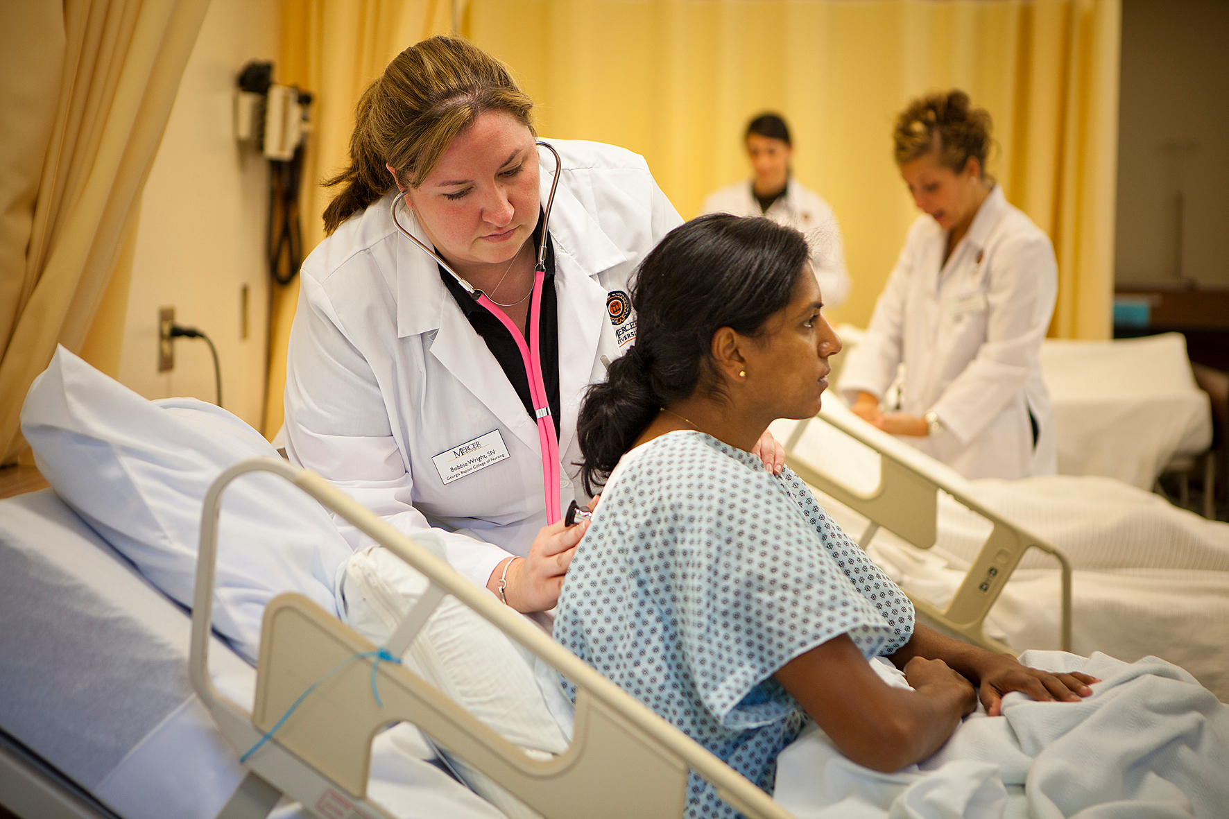 a woman wearing a white coat uses a stethoscope to check the lungs of a person sitting in a hospital bed