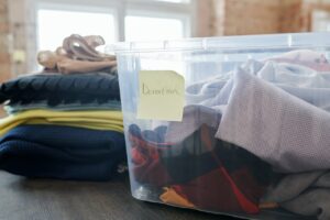 clothes are in a clear plastic tub. a yellow sticky note on the tub says donation