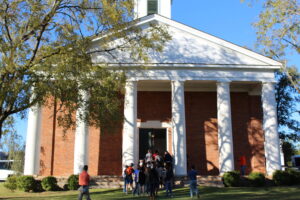 People walk through the doors of a stately brick building with columns that resembles a church.