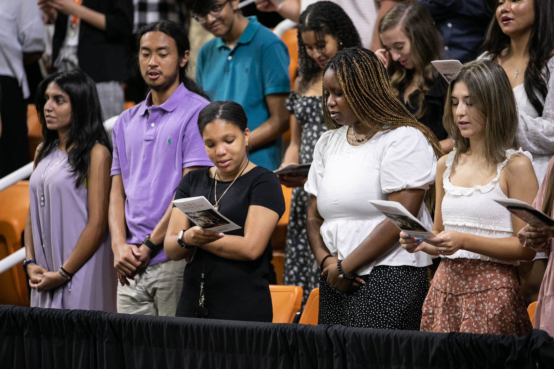 students stand while looking at the back of a program