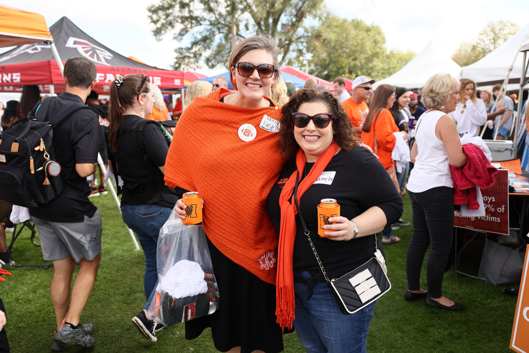 two women wearing orange and black smile amid other tailgaters on black field