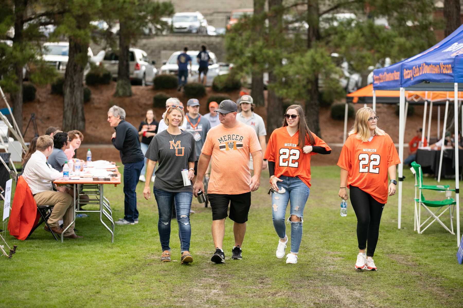 a man and woman wearing mercer shirts, and two young women wearing mercer jerseys, walk onto black field