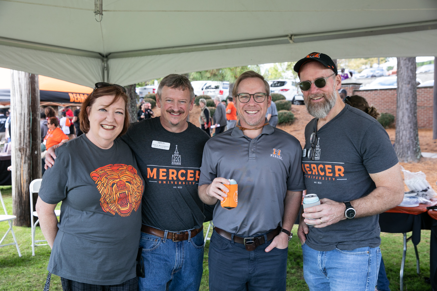 three men and one woman wearing mercer shirts smile at a tailgate
