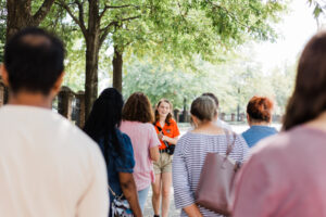 a college student wearing an orange shirt talks to a crowd of people