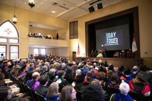 A large crowd seated in a room with a screen that says Founders' Day 2023.