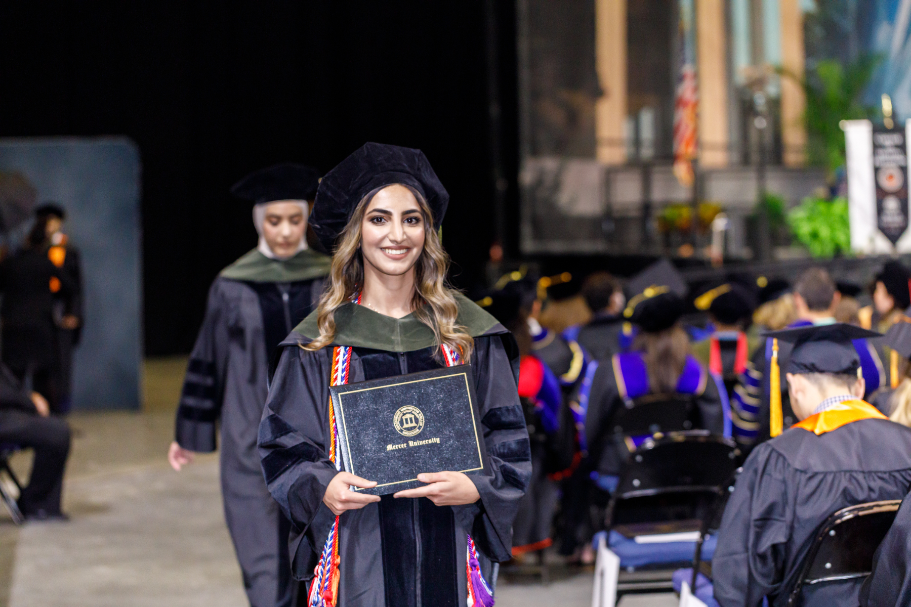 a woman wearing graduation regalia holds a diploma