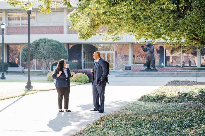 Two professionals engage in a conversation while walking on a pathway near a bear statue on Mercer's Atlanta campus.
