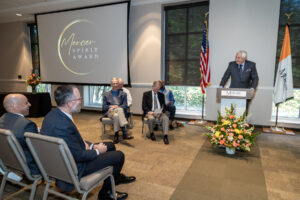 a man stands behind a podium, and the words mercer spirit award are projected on a screen to his left