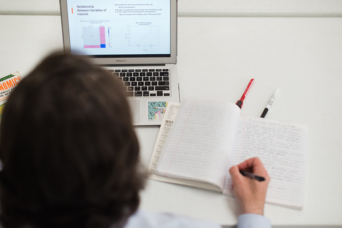 an overhead view of a person writing in a notebook while looking at an open laptop