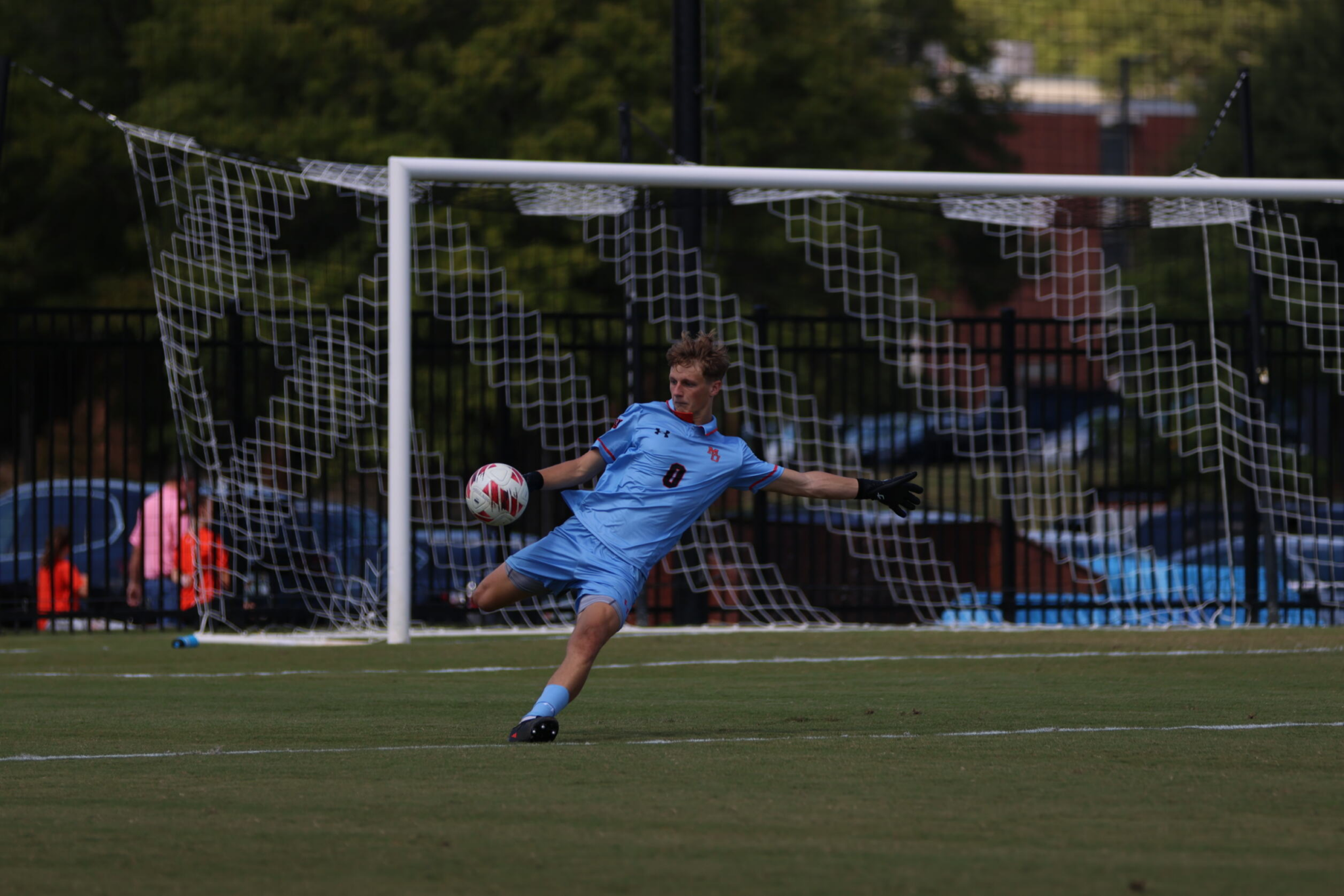 A soccer goal keeper in a Mercer uniform kicks away a ball during a match.