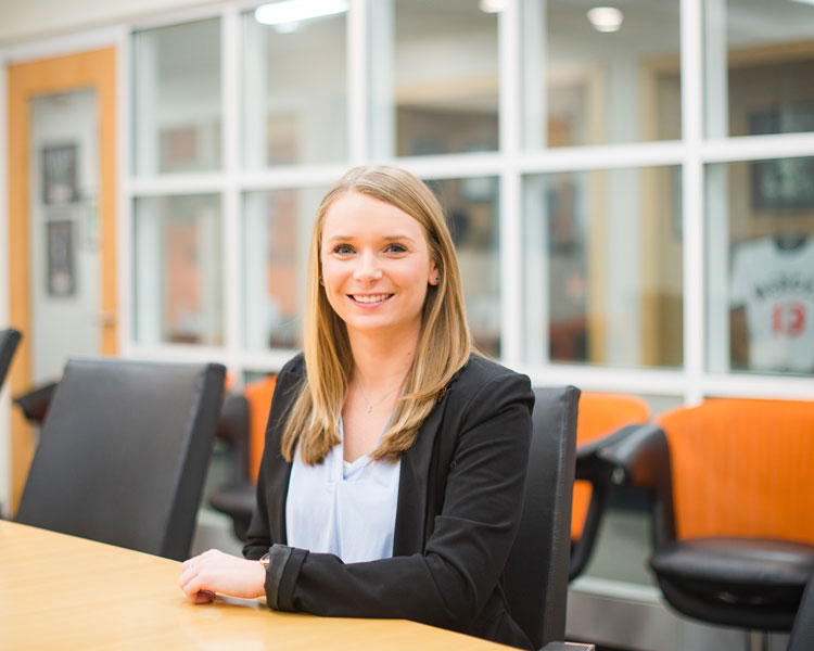 A young woman sits at a table and smiles at the camera.