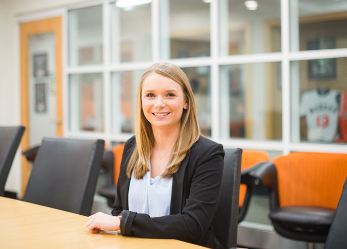 A young woman sits at a table and smiles at the camera.