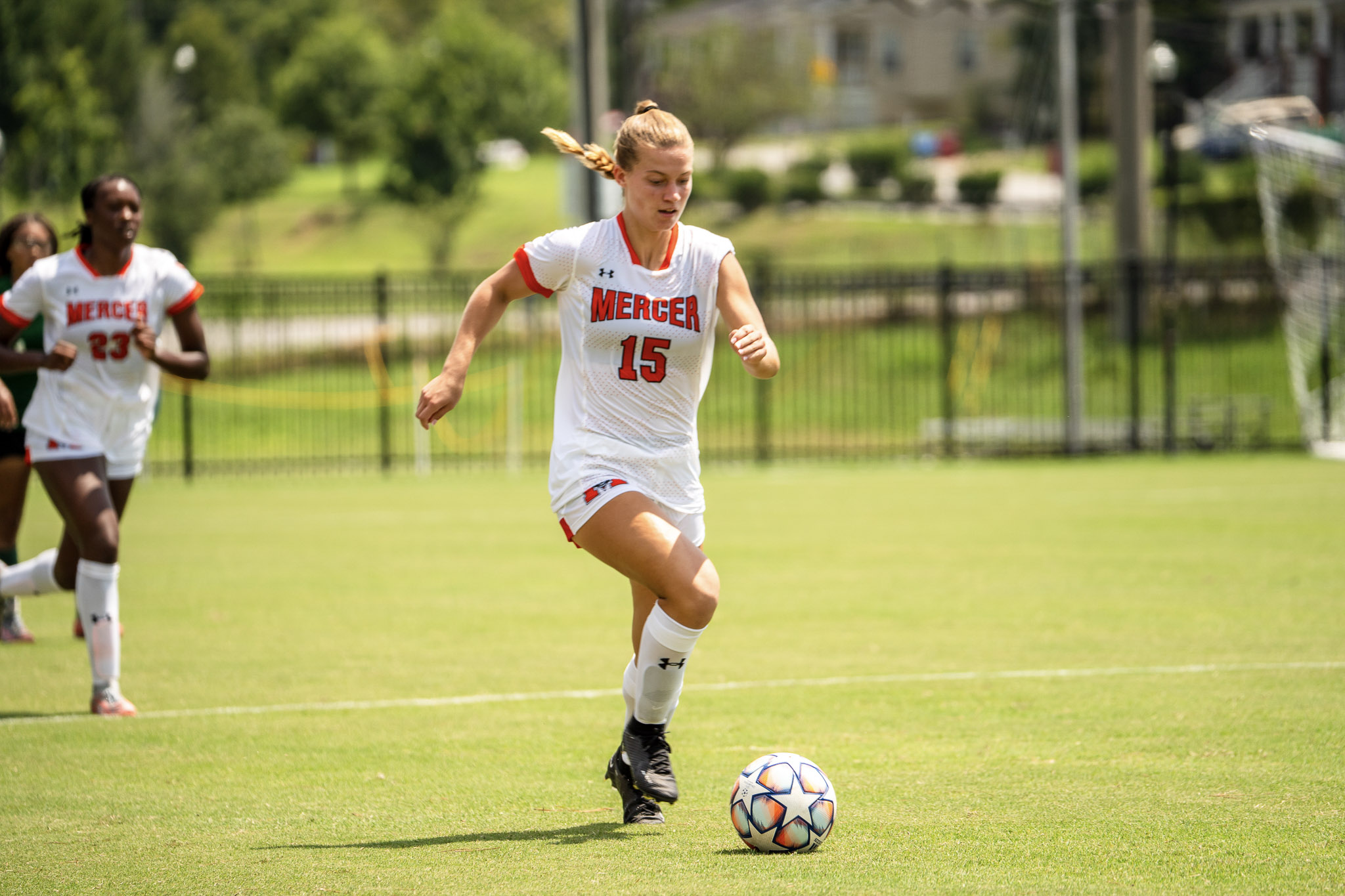 A Mercer women's soccer player dribbles a soccer ball down the field during a game, with another player in the background.