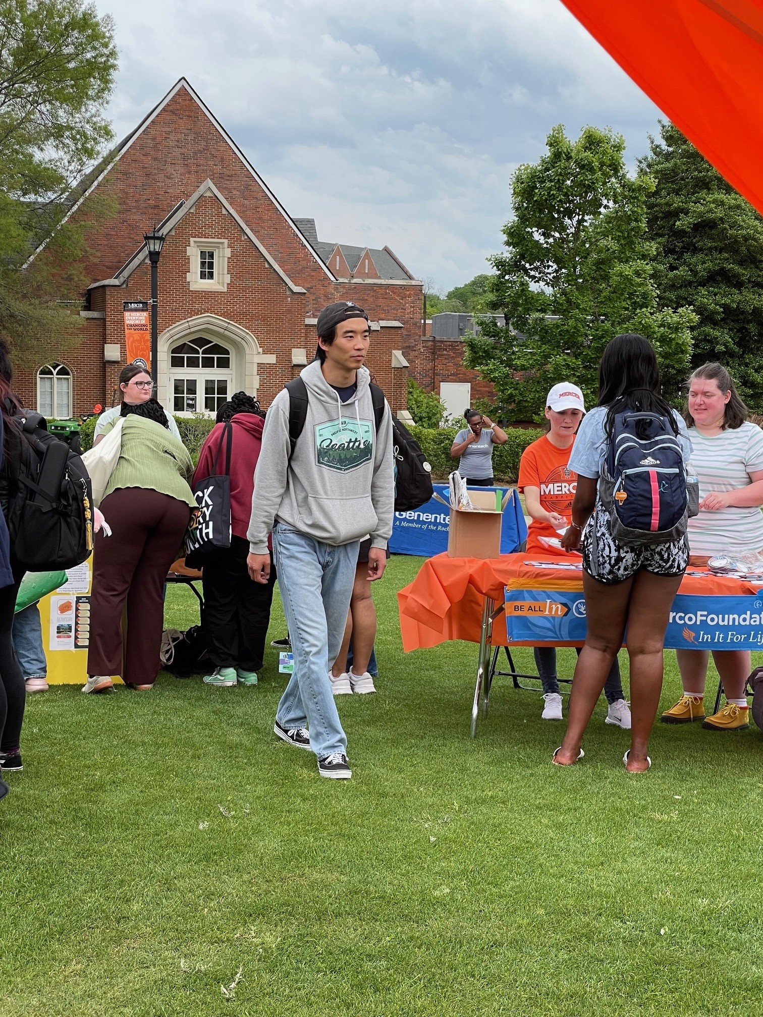 Students visit tables set up outside in a grassy area. A building can be seen in the background.