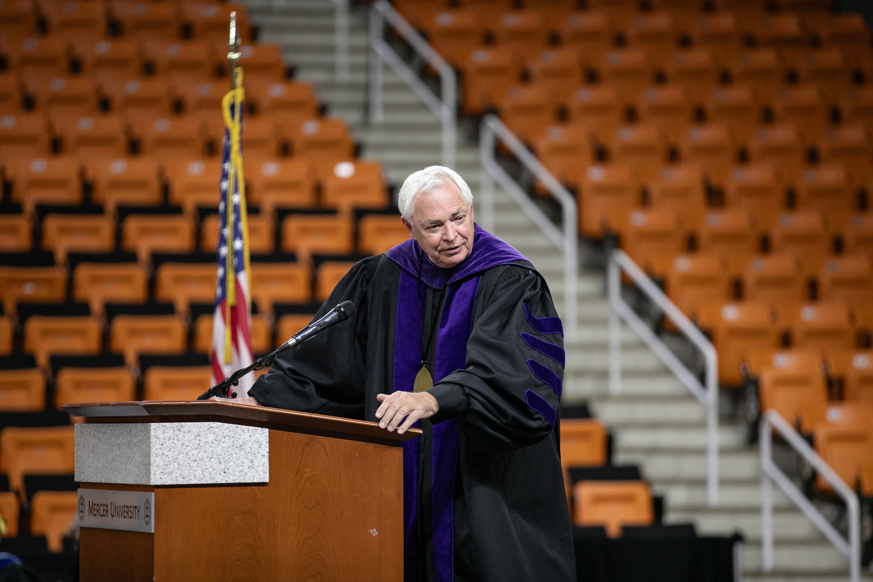 Mercer President William D. Underwood wearing academic regalia and standing behind a podium in Hawkins Arena.