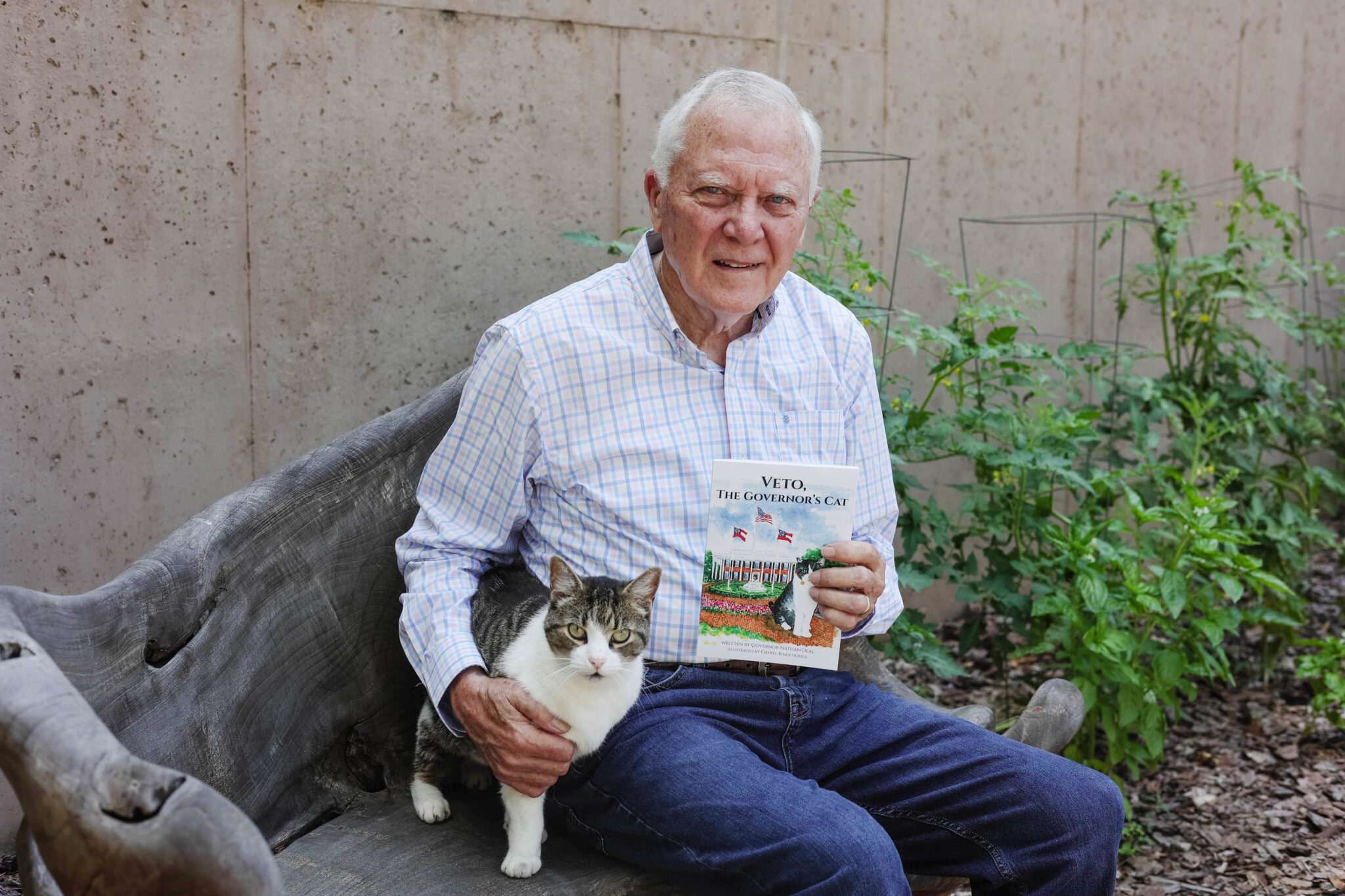 Nathan Deal sits on a bench next to a cat outside.