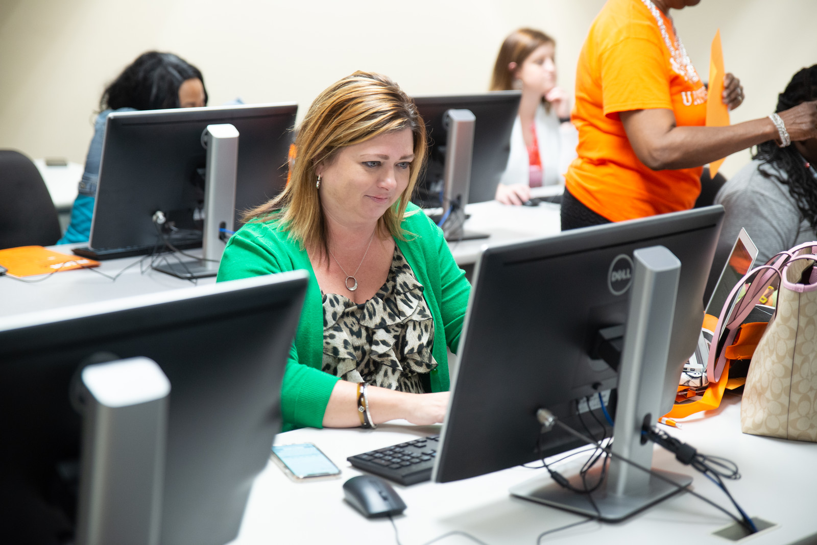 A woman sits in a classroom while typing at a computer.