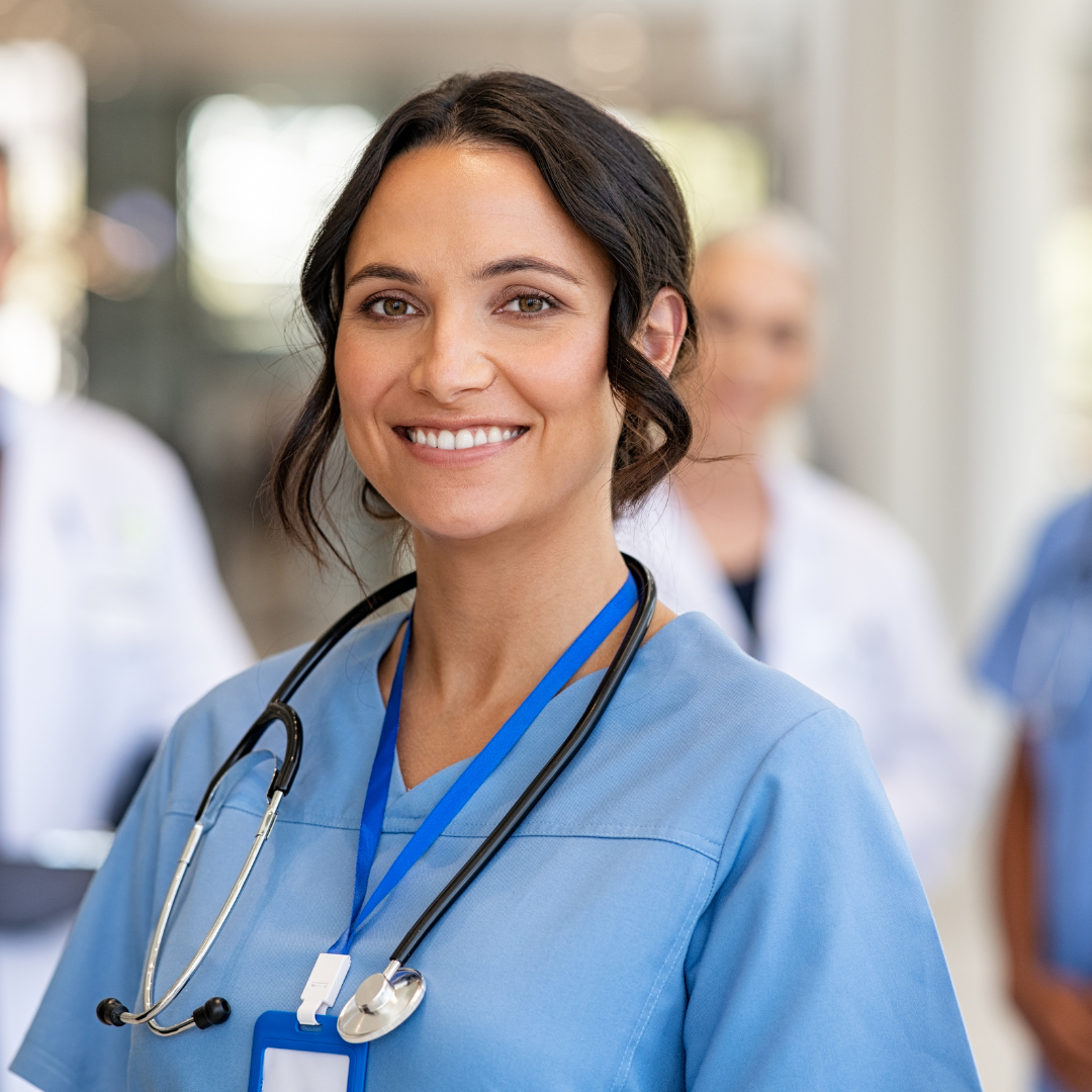 A nurse wears blue scrubs and has a stethoscope around her neck.