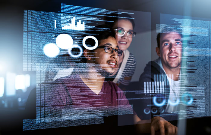 Three people analyze data visualizations projected in the air in front of them in a modern office setting. The visualizations include various graphs and circular diagrams.