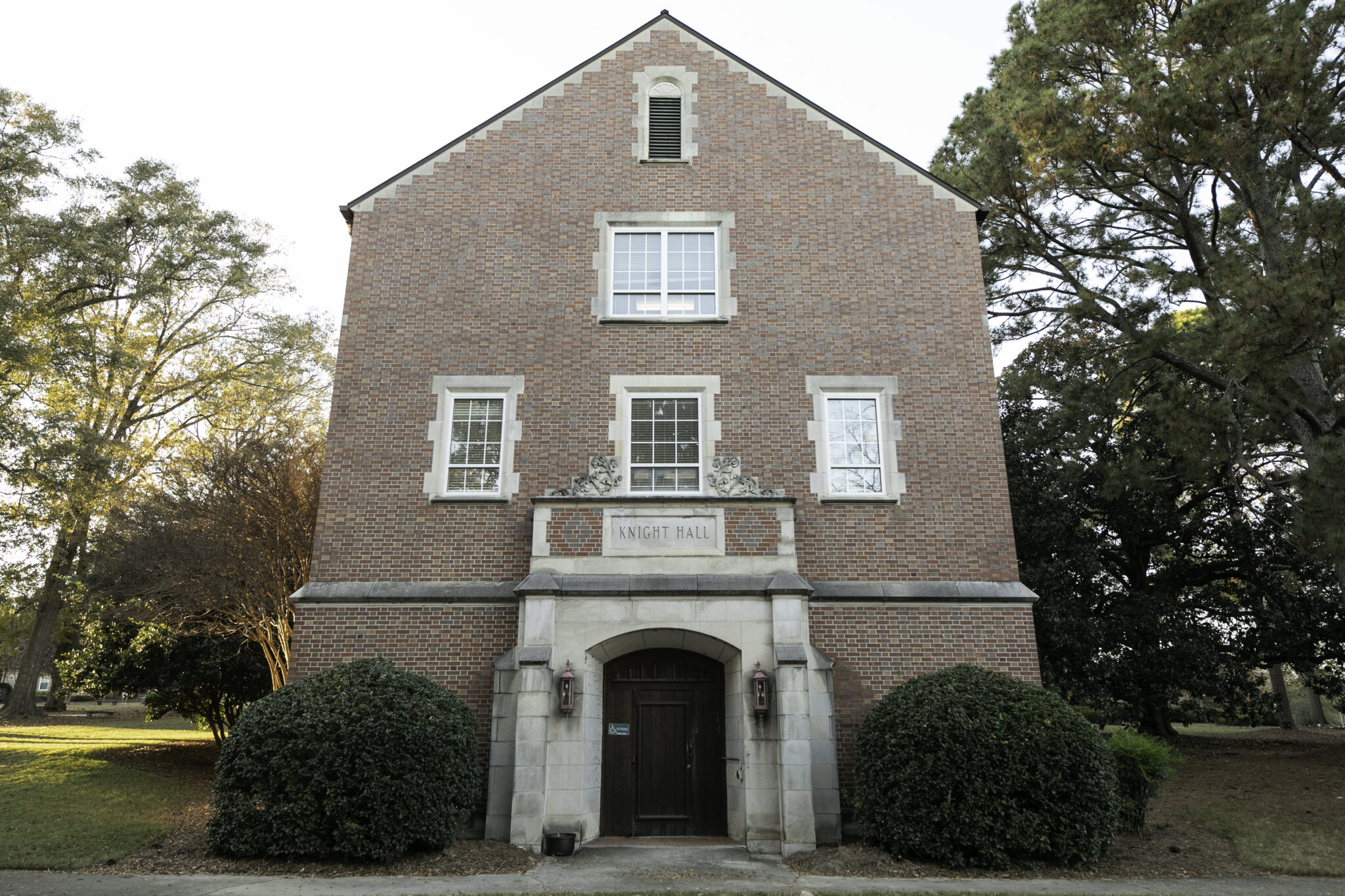 Exterior of Knight Hall, a three-story brick building with bushes on either side of the front door.