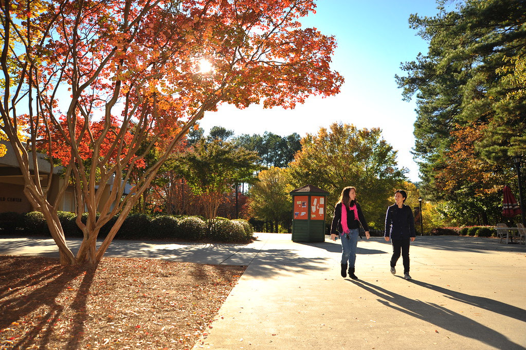 Two people walk on a college campus on a sunny, fall day.