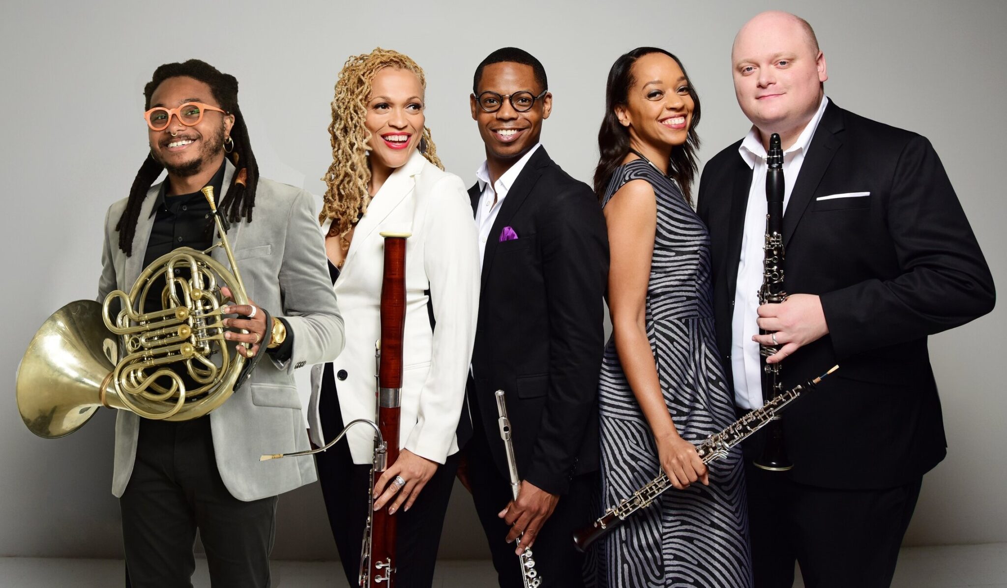 Five people in suits and dresses holding various instruments.