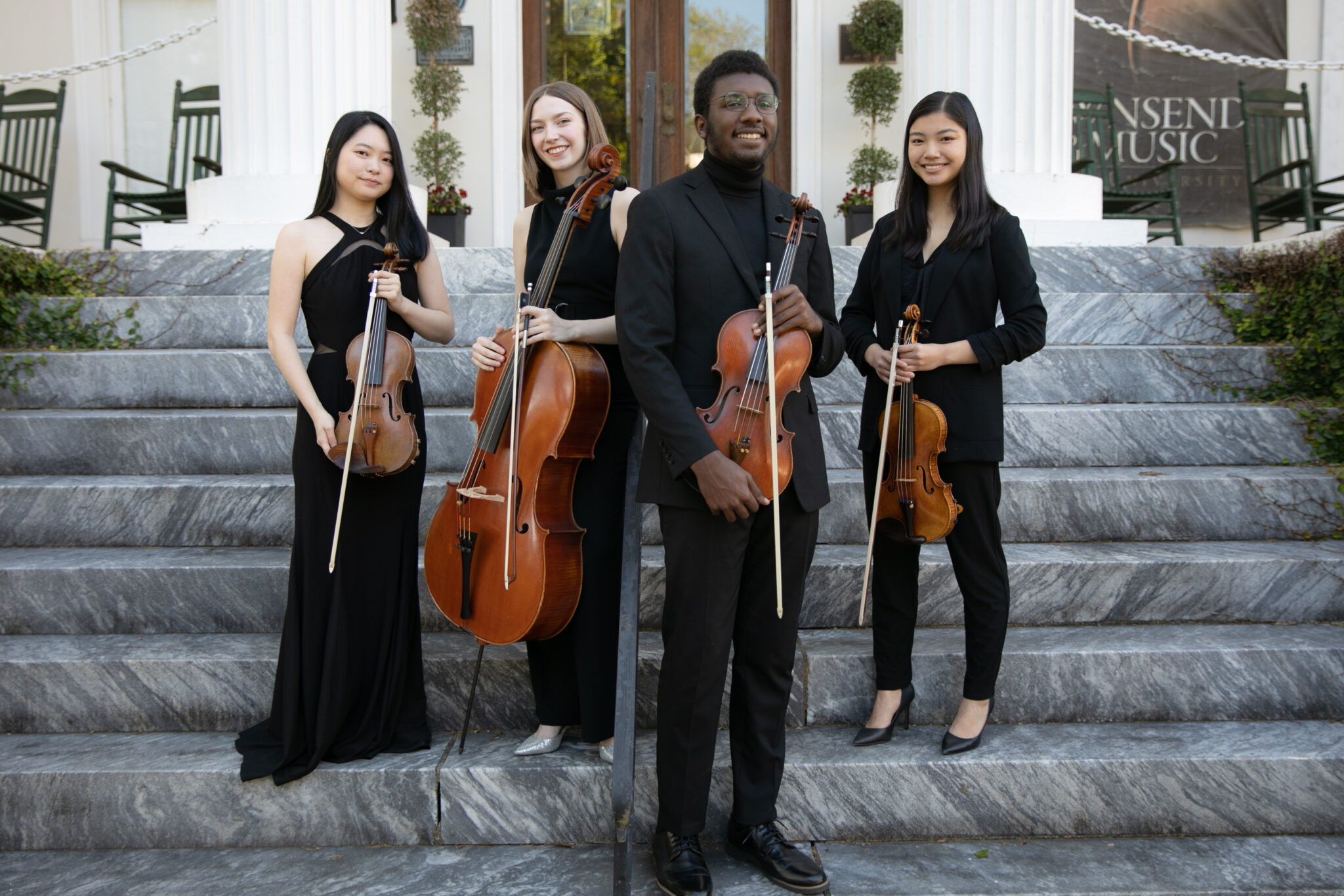 Four young people wearing all black hold various string instruments.