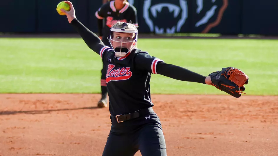 A softball player wearing a black Mercer uniform winds up to throw a pitch from the mound.