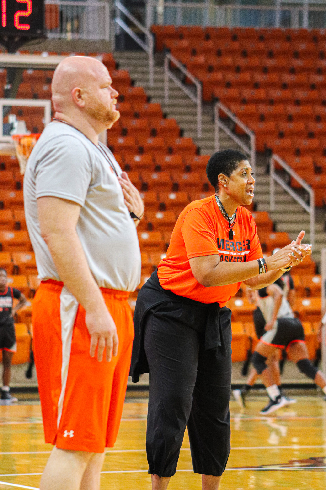 Mercer women's basketball head coach, wearing an orange Mercer T-shirt and black pants cheers on her team from the sidelines.