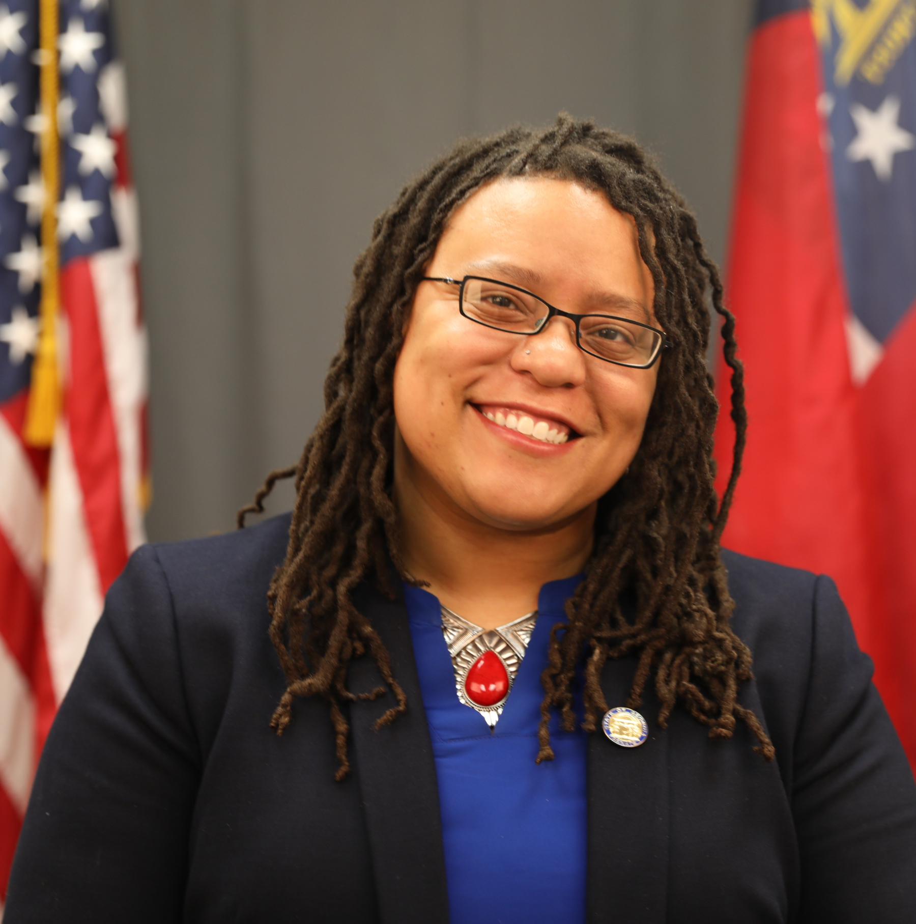 Headshot of Kim Jackson wearing a blue blouse and a navy blue blazer. An American flag and Georgia state flag are seen behind her.