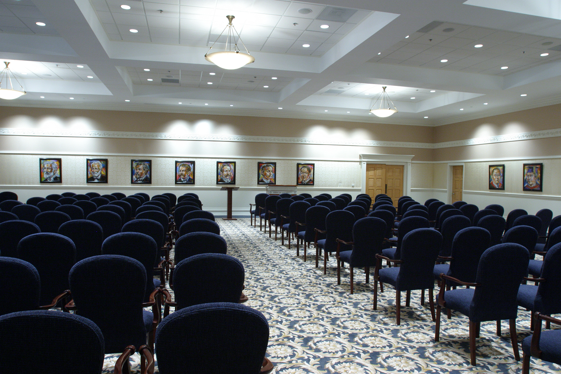 Rows of chairs are set up in a well lit room with paintings of Mercer presidents on the walls.