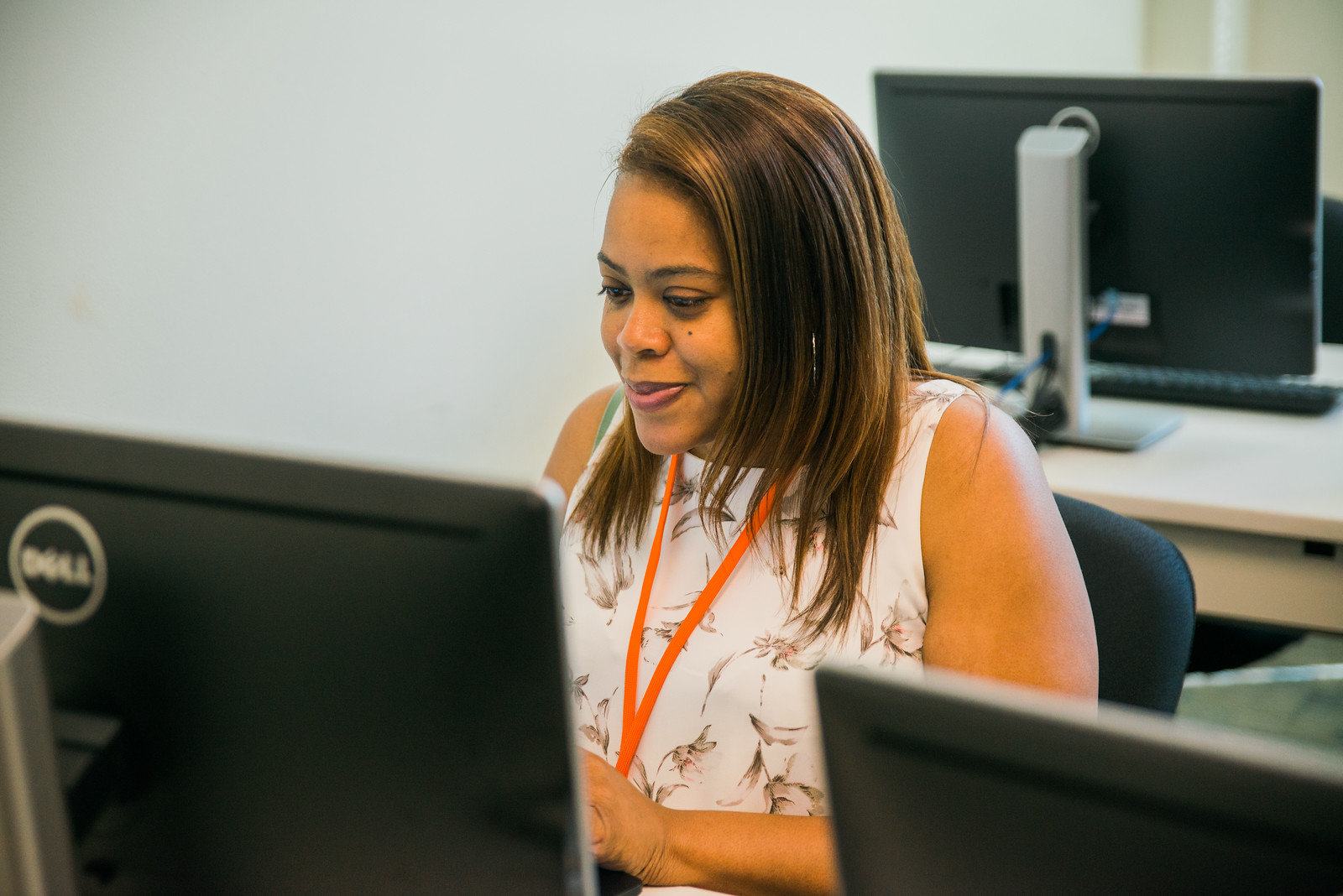 Person wearing an orange lanyard working at a desk with a Dell computer monitor in an office setting.