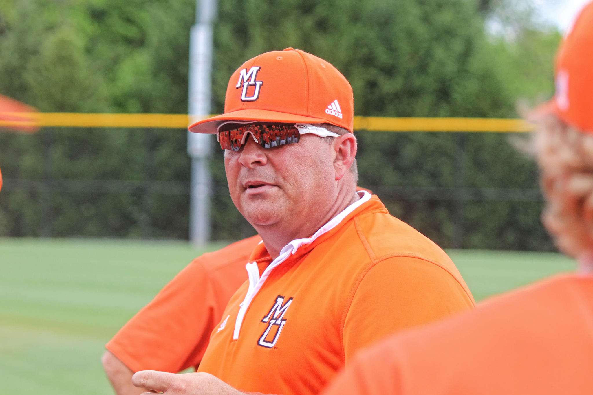 Mercer baseball coach Craig Gibson wearing an orange baseball cap and orange polo shirt. Both cap and shirt have an "MU" on them.