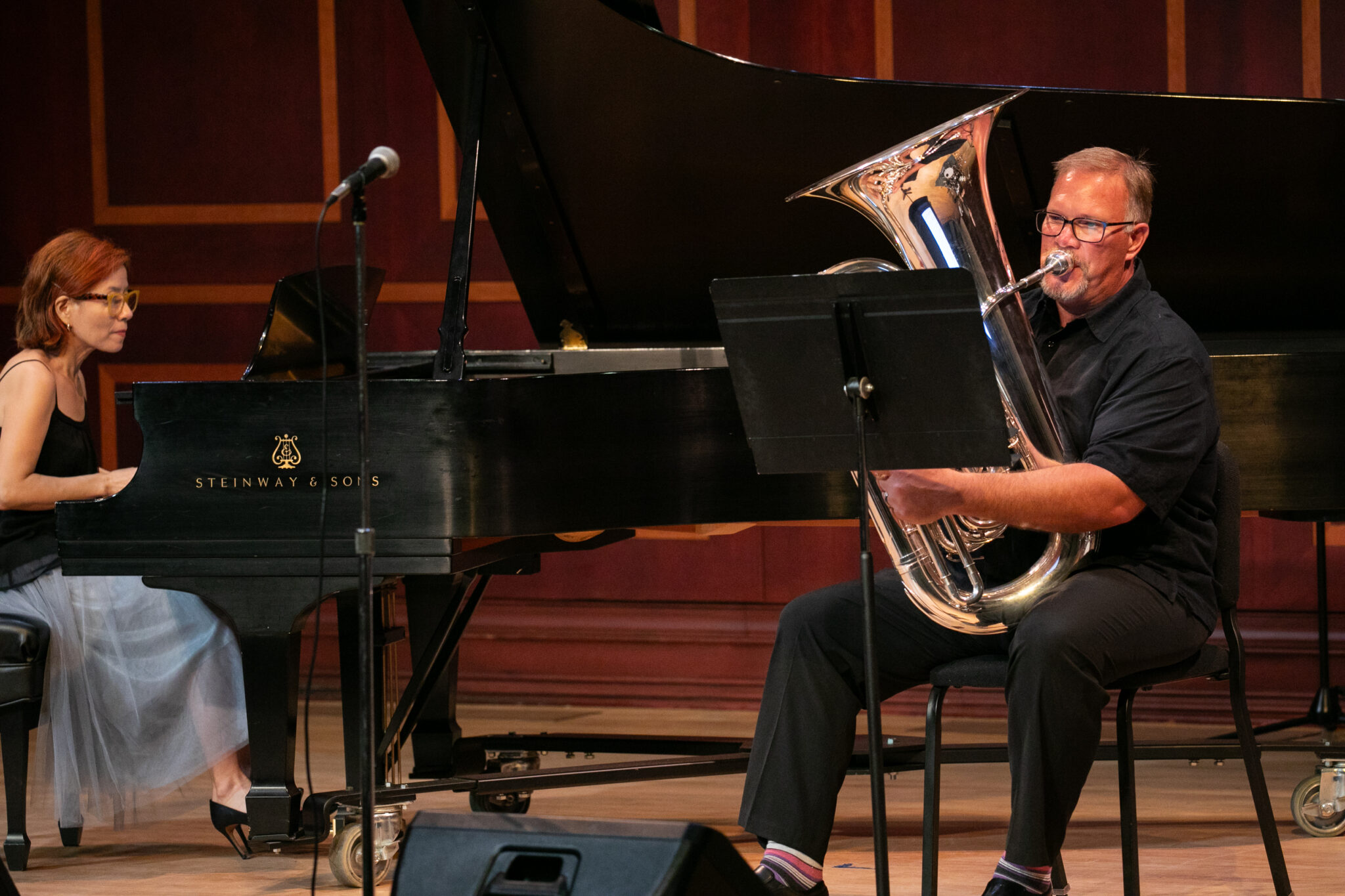 A musician plays a tuba while another musician plays a piano on stage.