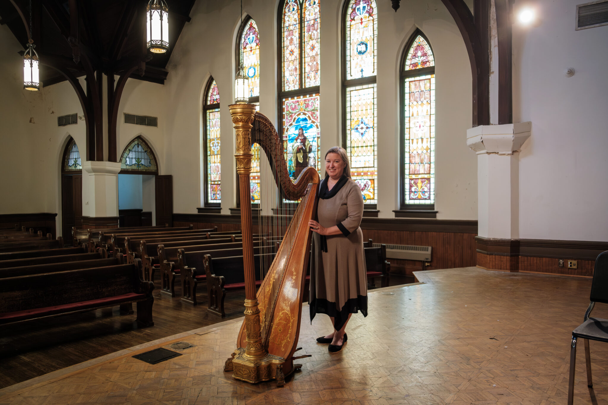 A woman standing behind a harp inside a chapel with colorful stained glass windows.