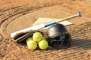 Softball balls, a glove, a bat and a helmet on the ground near home plate.