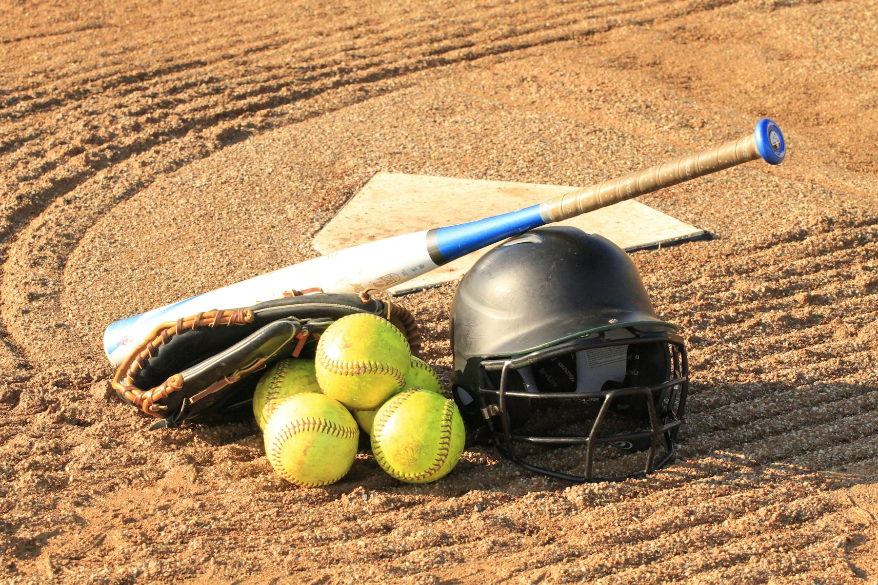 Softball balls, a glove, a bat and a helmet on the ground near home plate.