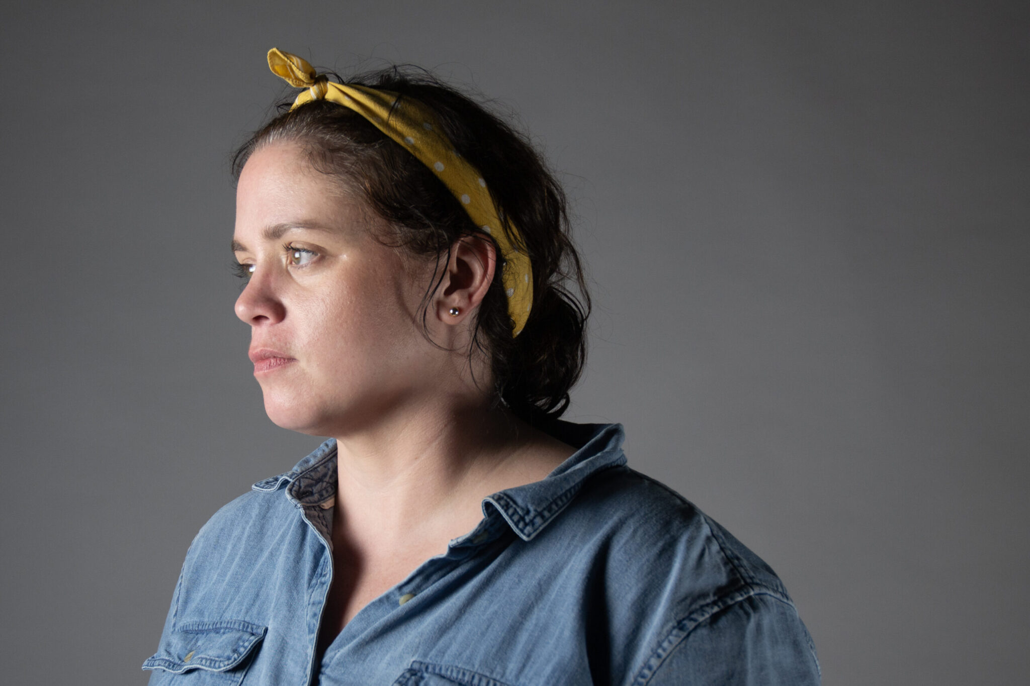 A woman in a yellow bandana and blue shirt looks off toward the left.