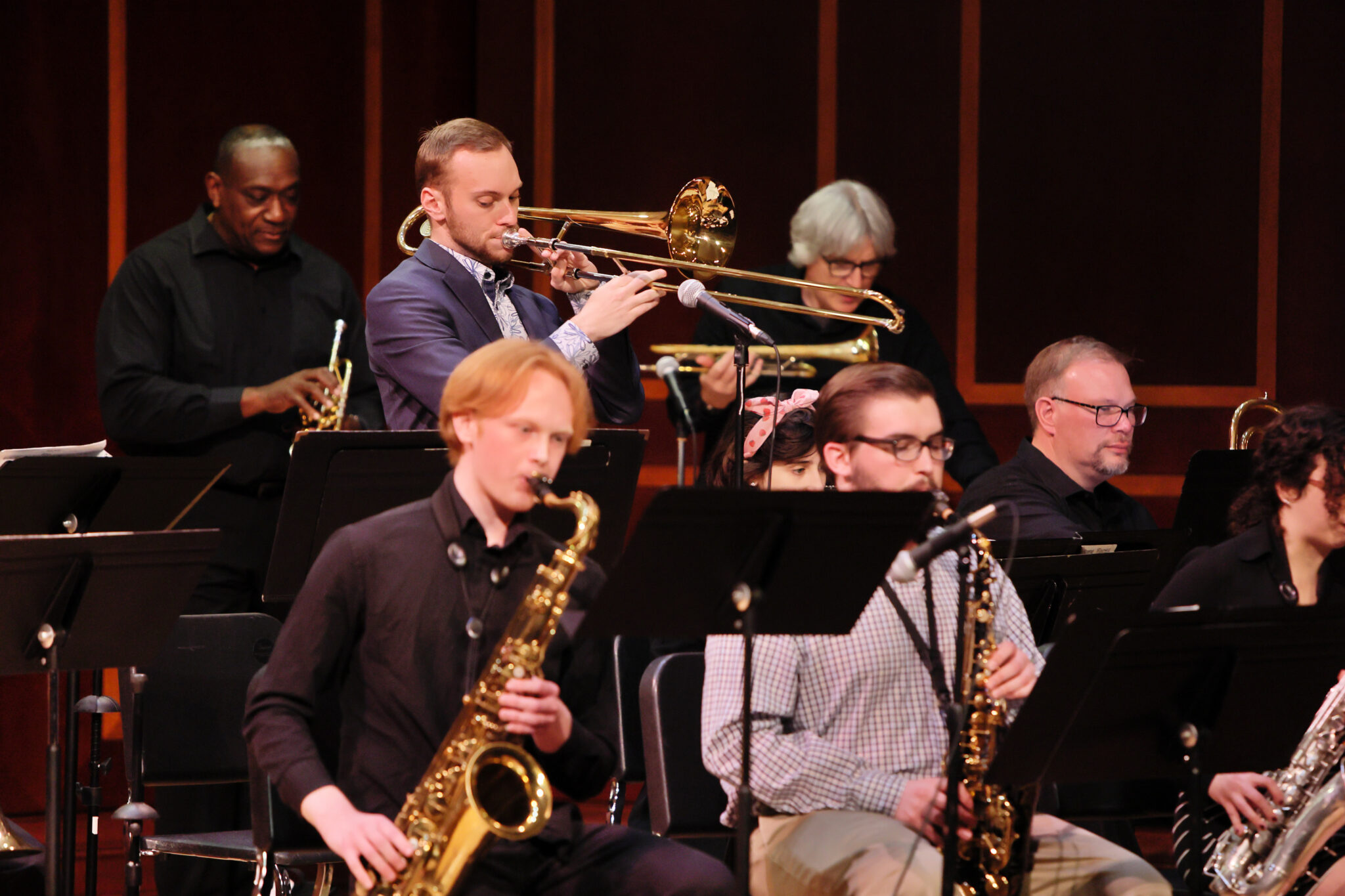 Musicians perform during a concert, featuring saxophones, trombones and trumpets.