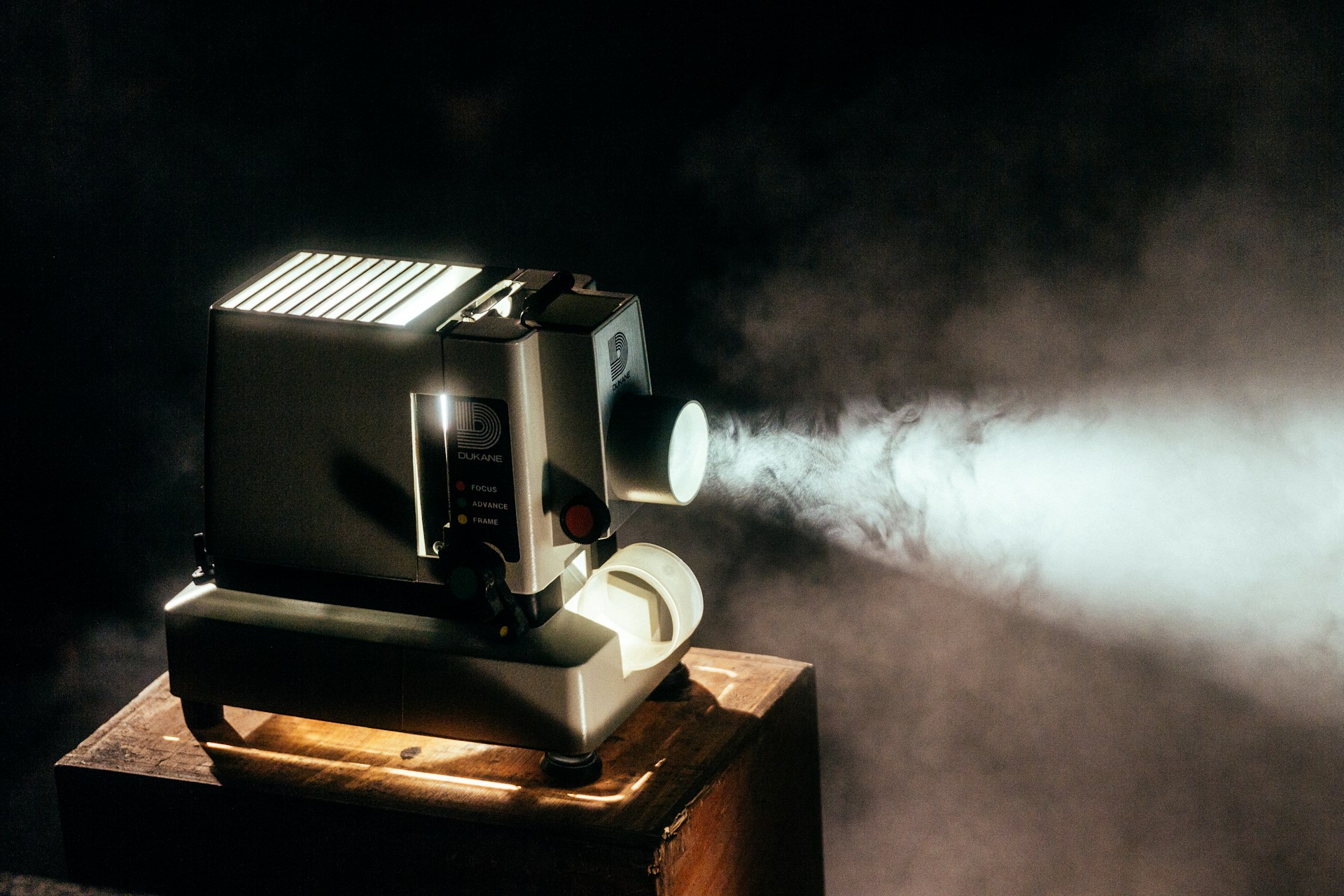 Vintage projector on a wooden table emitting light through smoke in a dimly lit room.