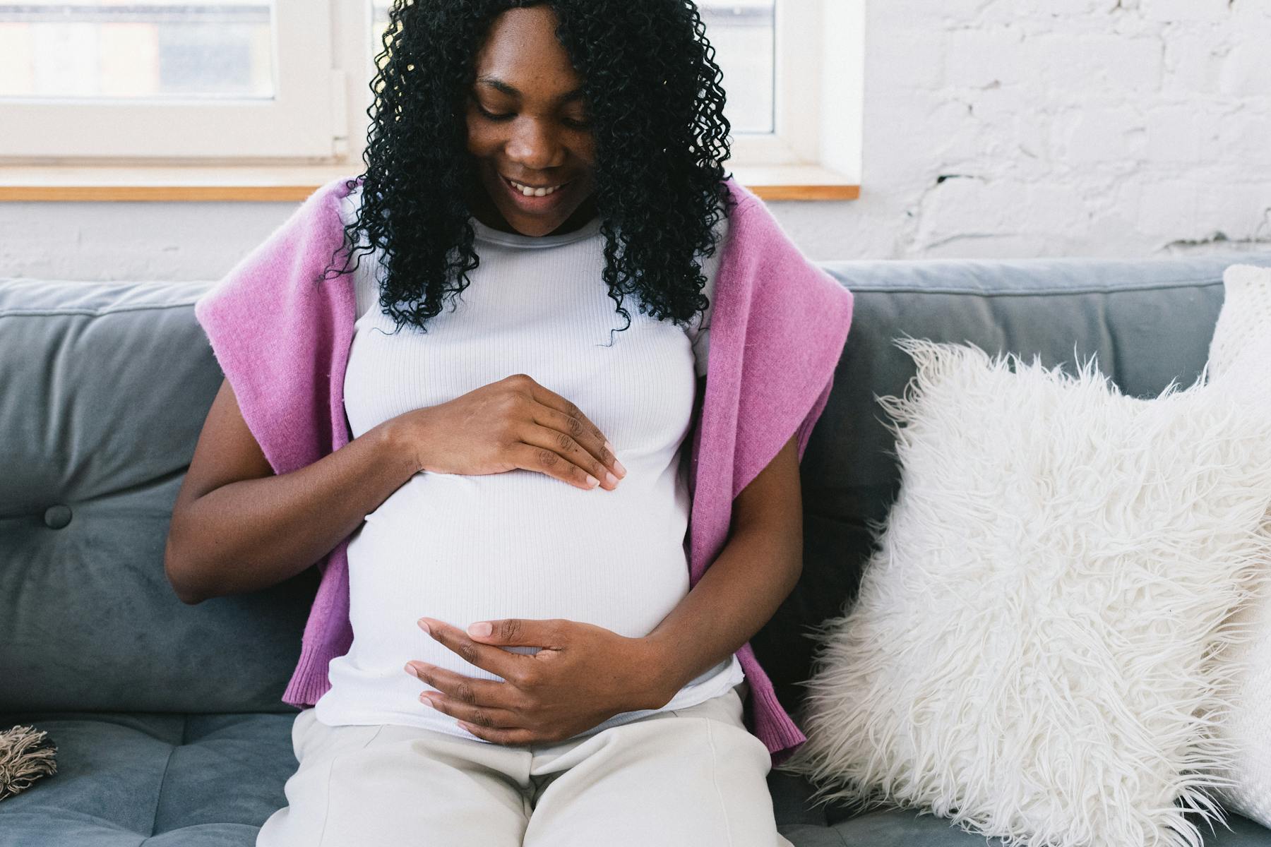 Happy pregnant black woman sitting on couch.