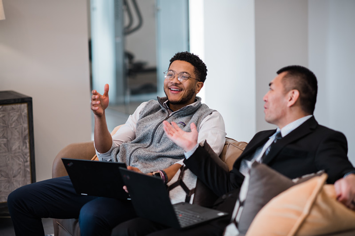 Two people interacting while seated on couch with laptops.