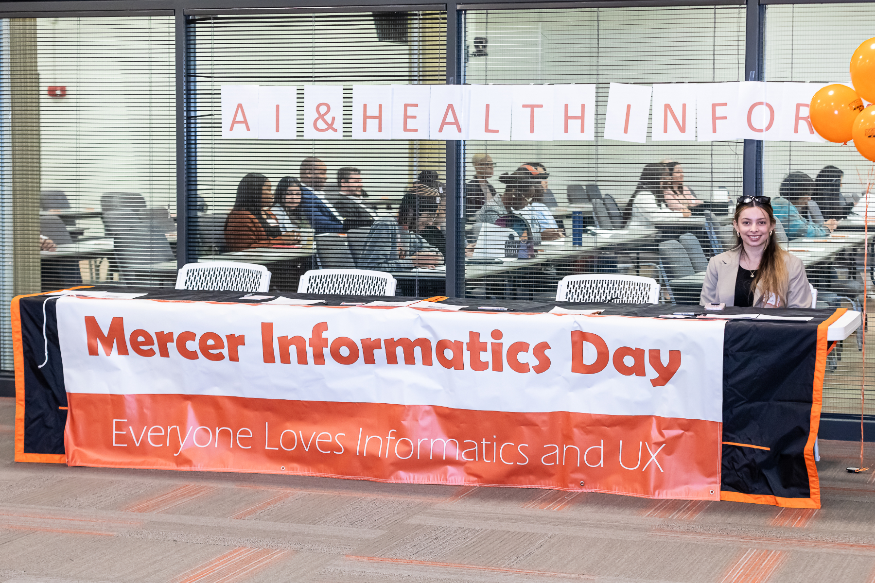 A woman sits at a table covered in a banner that reads, "Mercer Informatics Day."