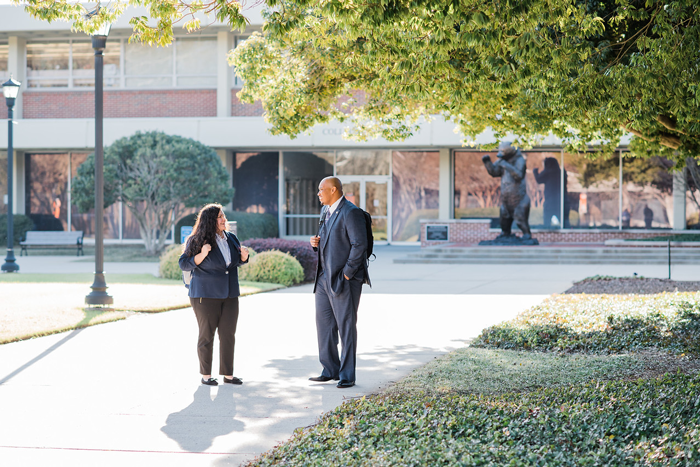 Two professionals engage in conversation while walking on a pathway near a bear statue on Mercer's Atlanta campus.