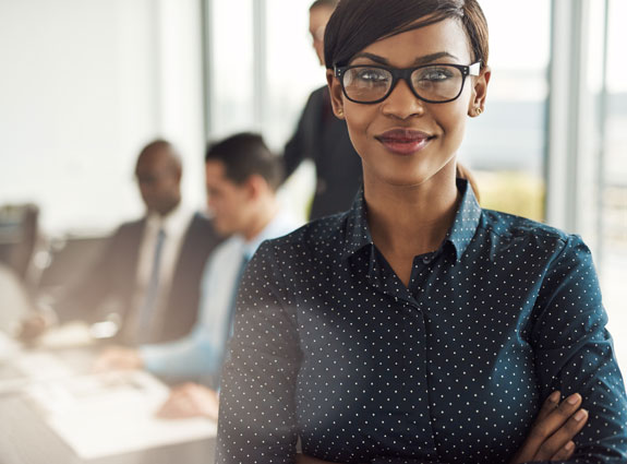 A confident professional stands at the foreground with a slight smile.