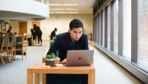 A Mercer student sitting at a desk works on a laptop.