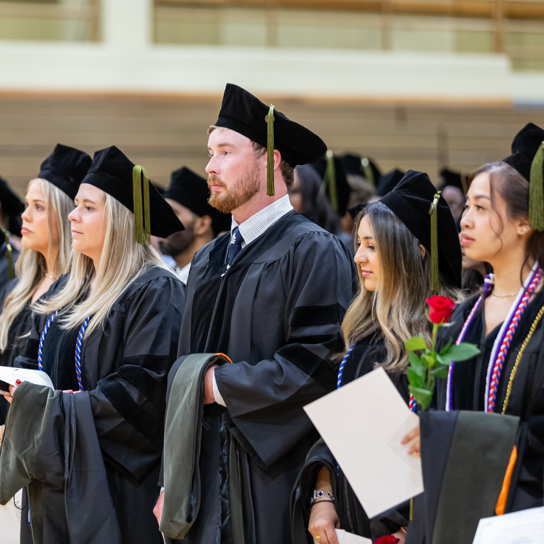 People in graduation caps and gowns stand in an auditorium.
