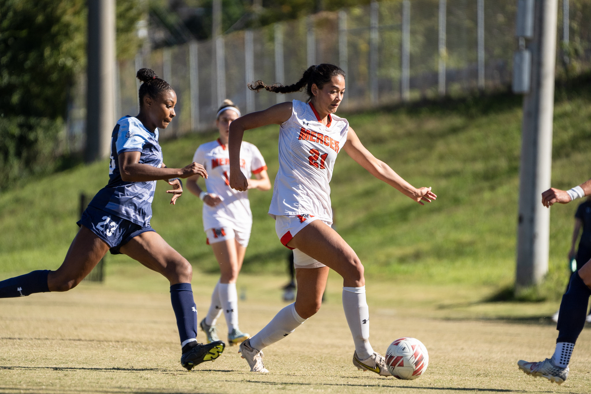 A Mercer women's soccer player dribbles the ball while being chased by an opponent.