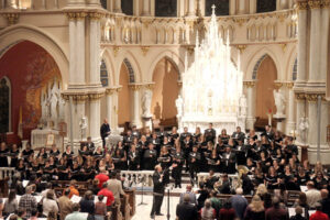 A choir performance inside a cathedral. A large audience is watching as the conductor leads the choir.